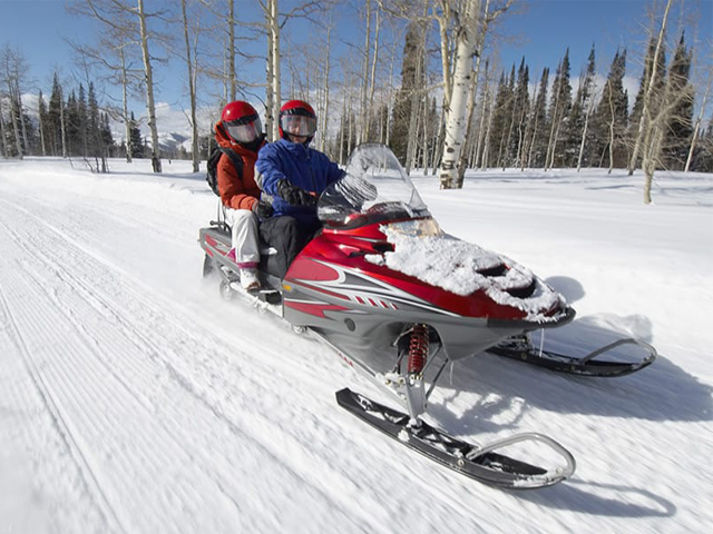Безопасное катание на снегоходе по зимней трассе. Фото двух людей в зимней спецодежде и снегоходном шлеме во время езды на снегоходе